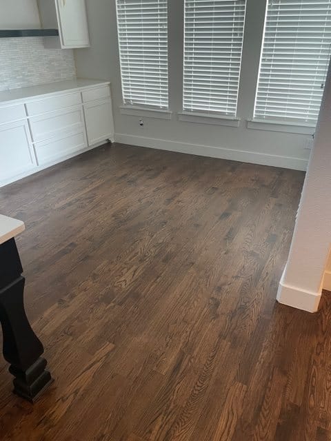 dark hardwood flooring, three windows and white cabinets